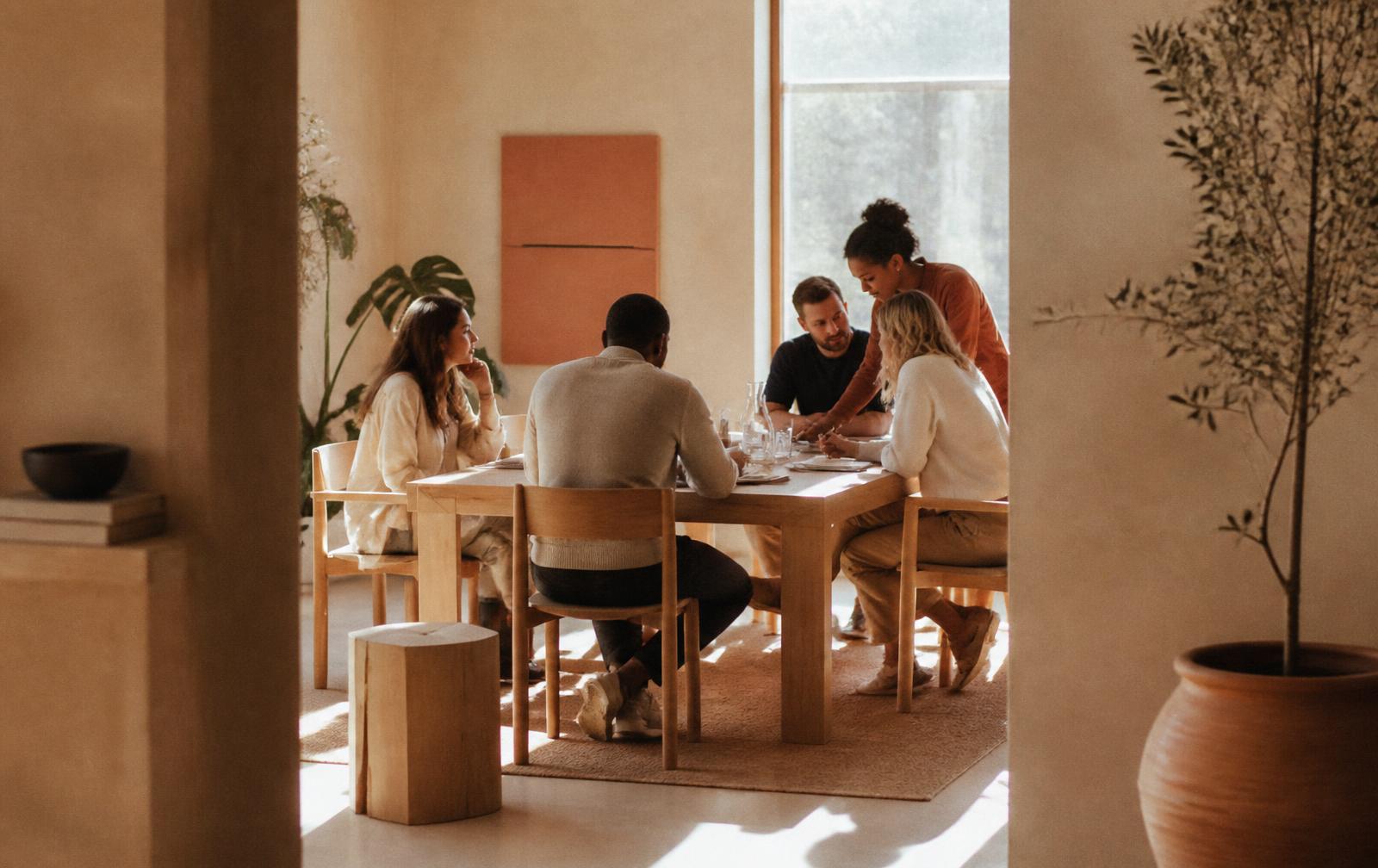 A small group of colleagues reviewing work together at a wooden table in a sunlit room